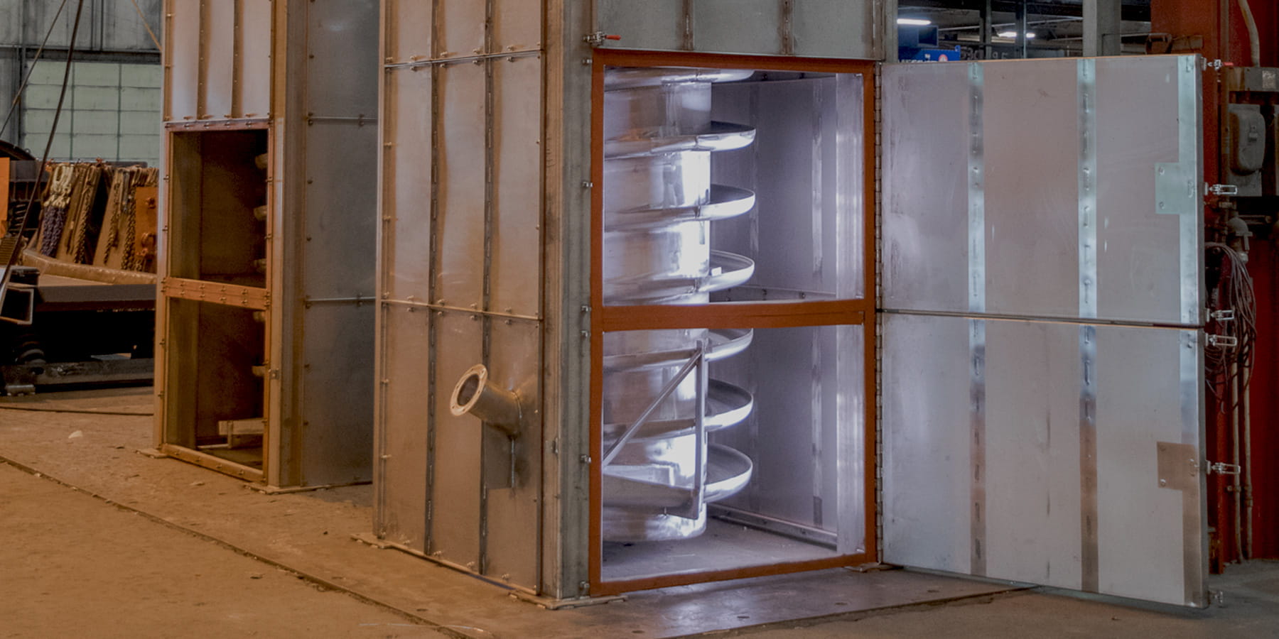 Industrial machinery with a large metallic chamber and exposed spiral blades inside, set in a factory floor scene.