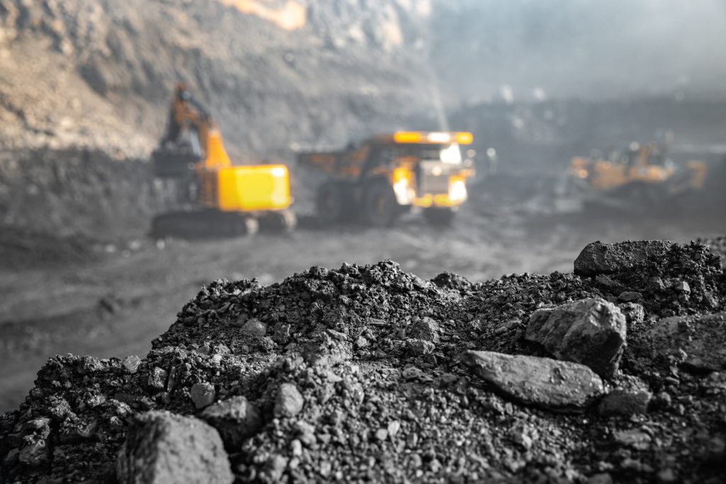 Mine de charbon à ciel ouvert. À l'arrière-plan, une excavatrice charge des minéraux anthracite dans un grand camion jaune.