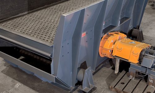 Gray industrial vibrating screen with perforated deck and an orange drive motor mounted on the side in a workshop setting