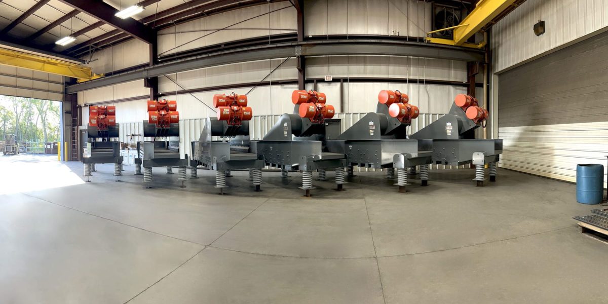 Row of large industrial machines with red motors on spring-loaded bases inside a warehouse.