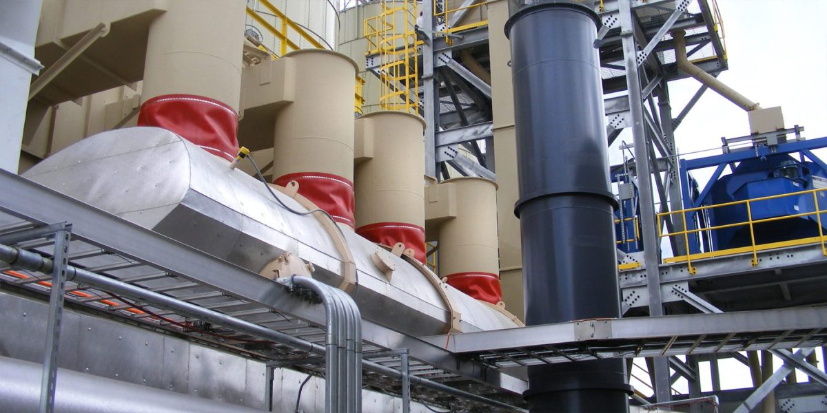Industrial industrial facility with beige insulated columns, red-capped ducts, and surrounding steel framework with yellow railings and blue machinery