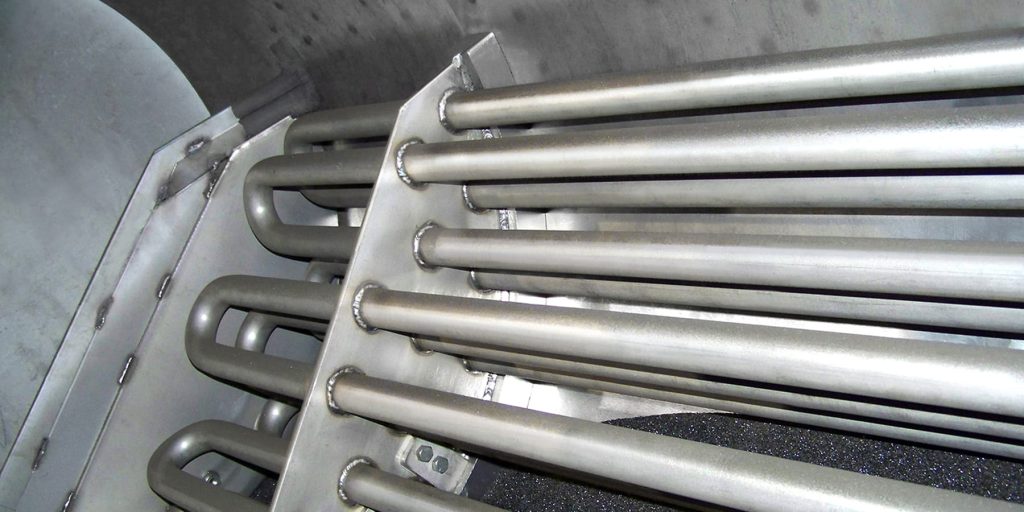 Close-up of parallel metallic tubes welded to a plate inside an industrial enclosure