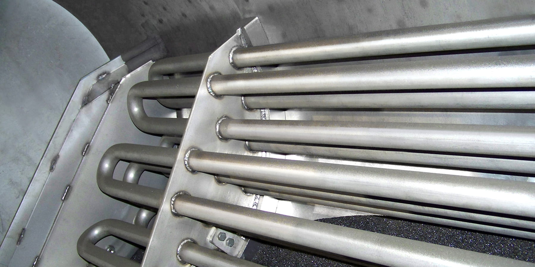 Close-up of parallel metallic tubes welded to a plate inside an industrial enclosure