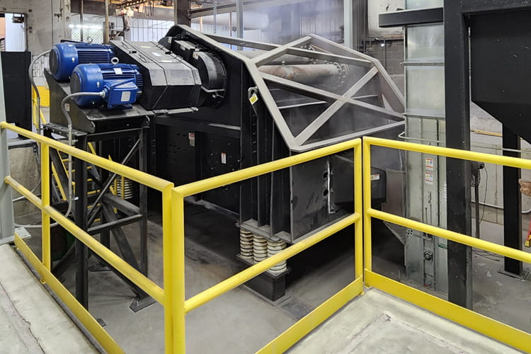 Industrial metal shredder with blue motors and a steel frame inside a factory, surrounded by yellow safety railing.